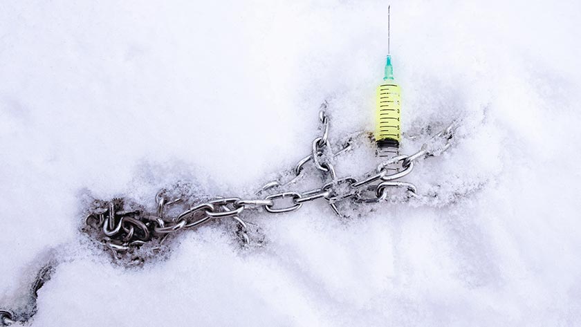 Metal chain in ice, accompanied by a syringe full of vaccine