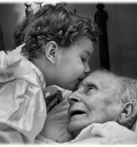 Small child kissing their aged bedridden grandparent on the forehead