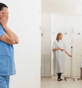 Nurse standing in a hospital corridor, covering her face in her hands